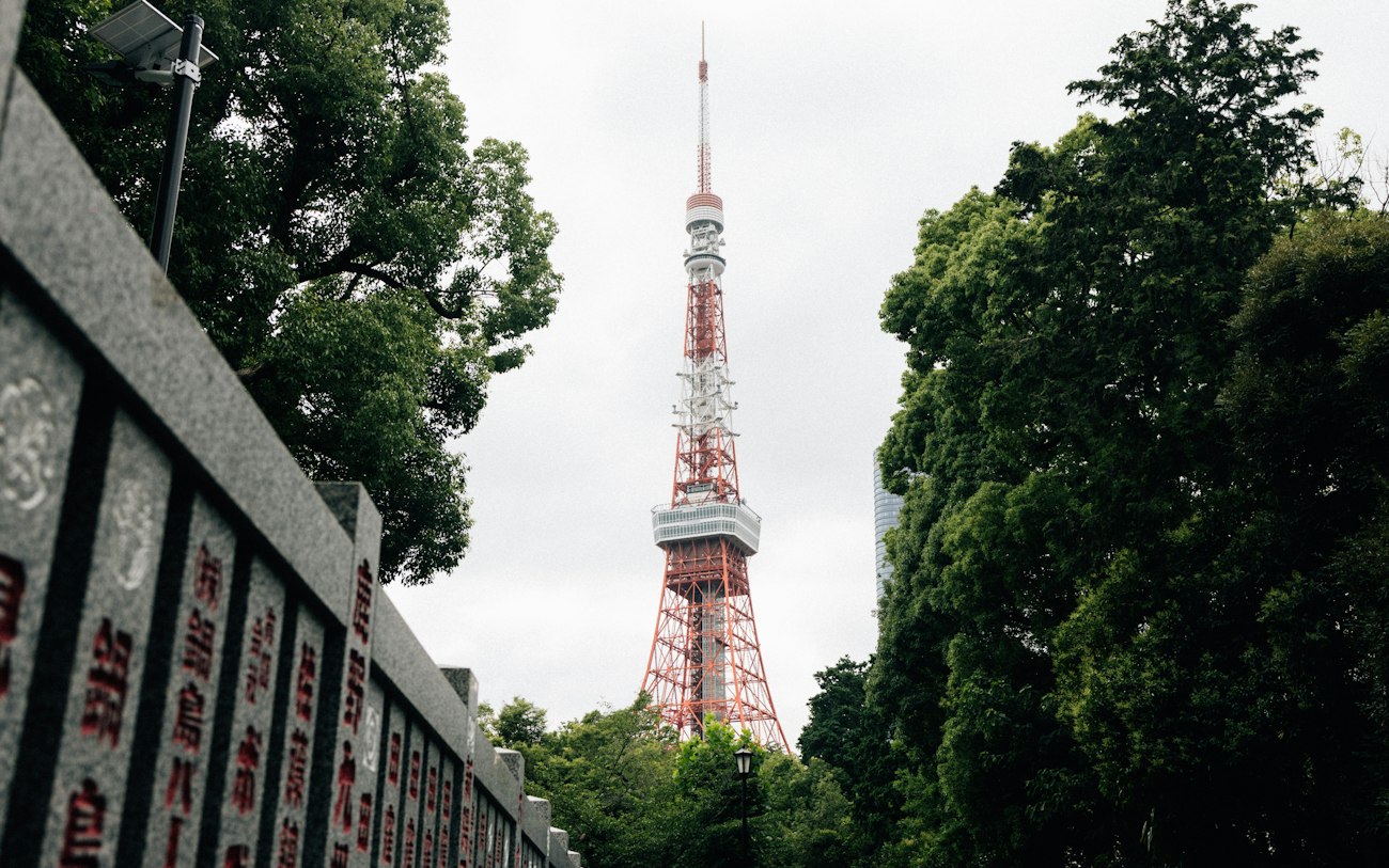 Der Tokyo Tower, eingerahmt von Bäumen und einer Steinmauer